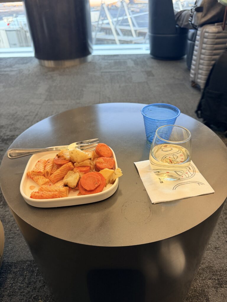 A plate of vegetarian pasta and a drink sit on a table in the lounge.