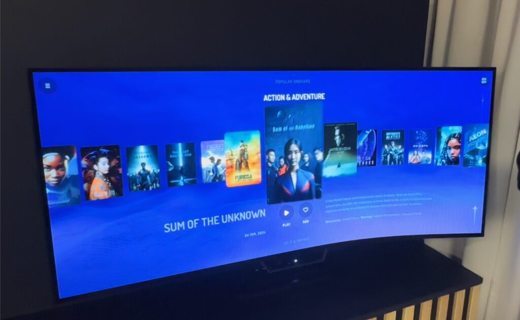 Different movie titles are displayed on the ultra-wide curved screen