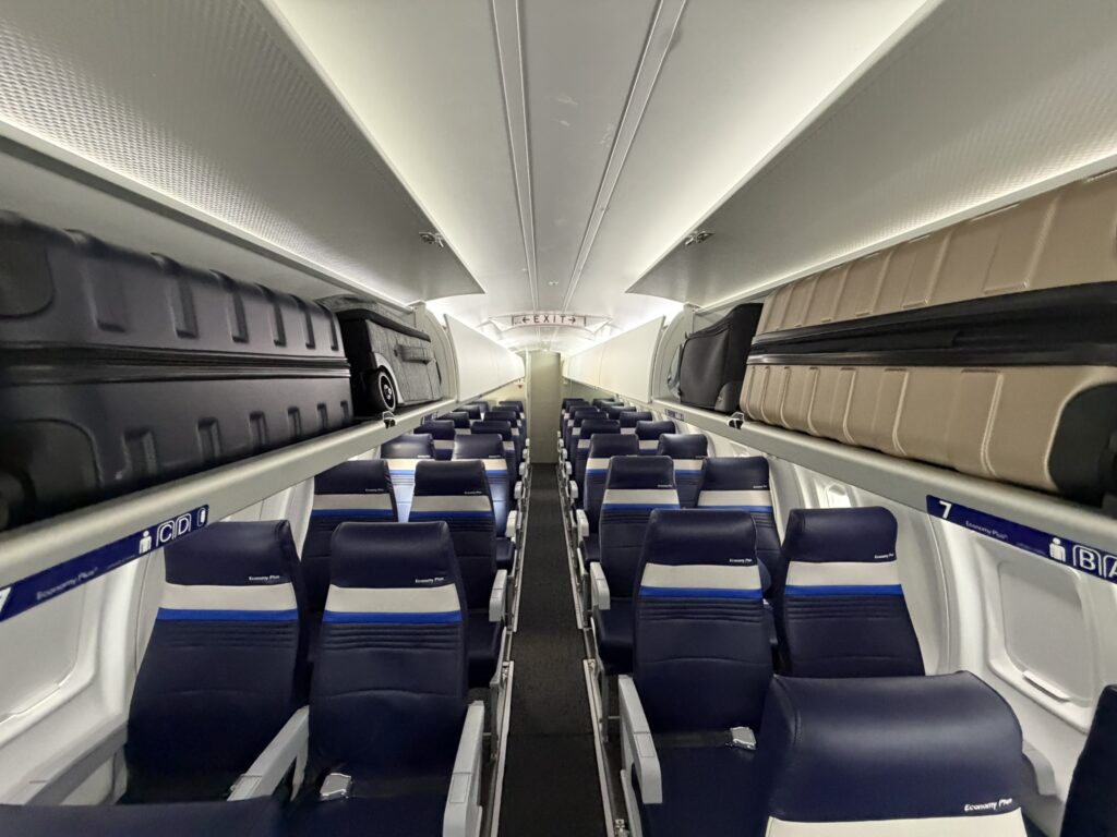 Inside the aircraft's economy cabin. The seats are mostly deep blue with white and lighter blue striped accents.