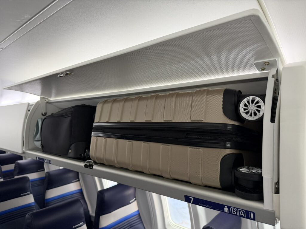 Two large bags are stowed in the overhead bin in economy class. 