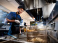 A man is cooking in an industrial kitchen at the grill.