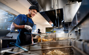 A man is cooking in an industrial kitchen at the grill.