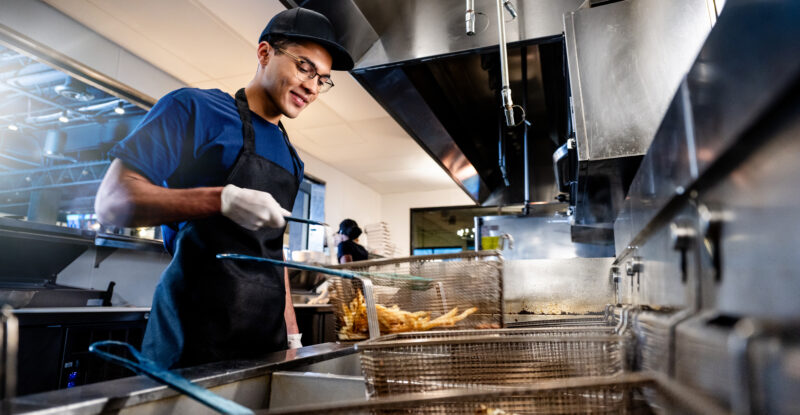 A man is cooking in an industrial kitchen at the grill.