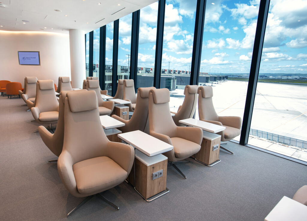 SkyTeam FRA Lounge shows large beige chairs in a room with lots of natural light coming from floor to ceiling windows.