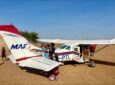 Rachel Gardner-Poole OBE in front of an aircraft with young children in Africa.
