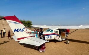Rachel Gardner-Poole OBE in front of an aircraft with young children in Africa.