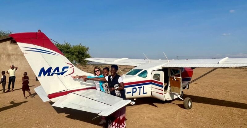 Rachel Gardner-Poole OBE in front of an aircraft with young children in Africa.