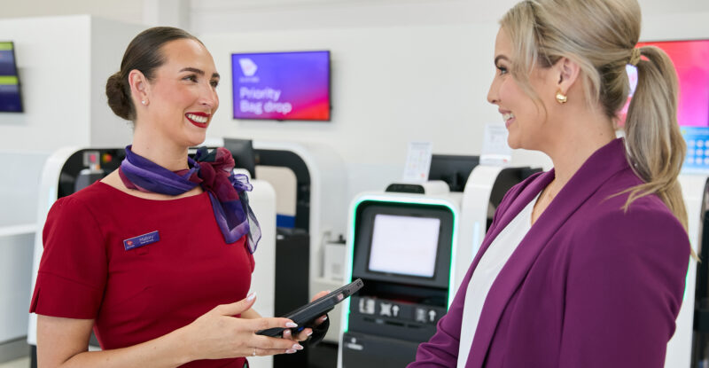 A Virgin Australia crew member is aiding digital check-in of a passenger.