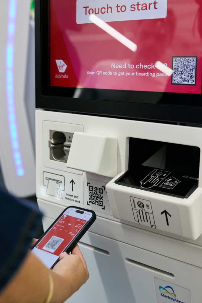 A close up of a passenger using their mobile device and the Virgin Australia bag tag kiosk.