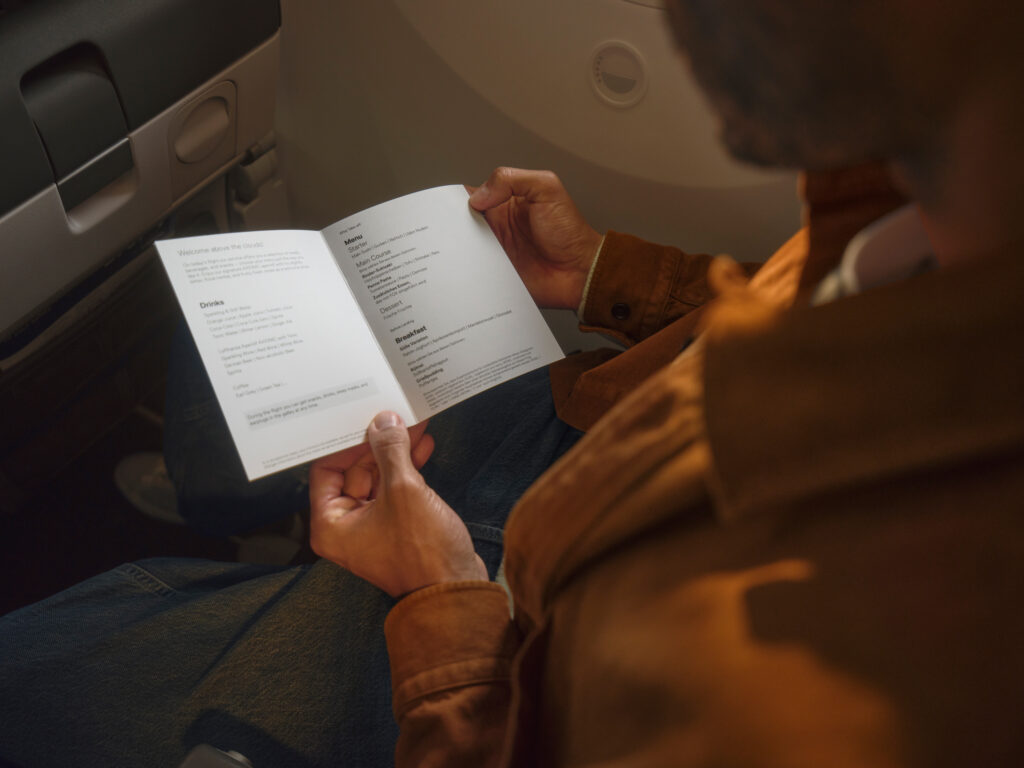 A passenger is reading a paper menu in flgiht.