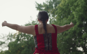 An Indigenous woman is wearing a red dress during a memorial ceremony.