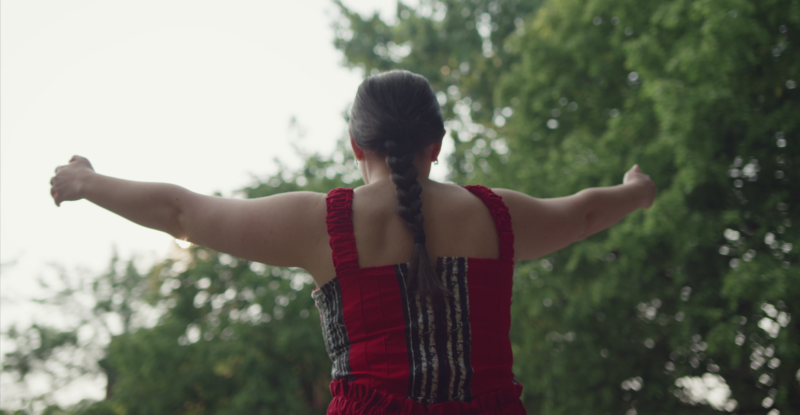 An Indigenous woman is wearing a red dress during a memorial ceremony.