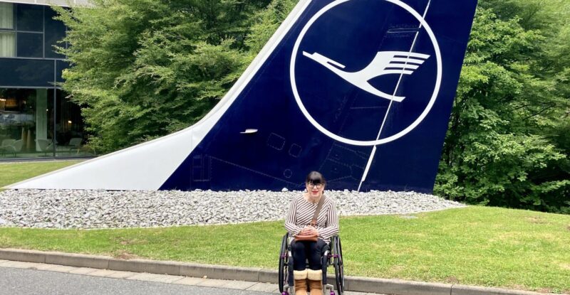 Mary Doyle posing for a photo in front of a Lufthansa aircraft tail.
