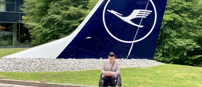 Mary Doyle posing for a photo in front of a Lufthansa aircraft tail.