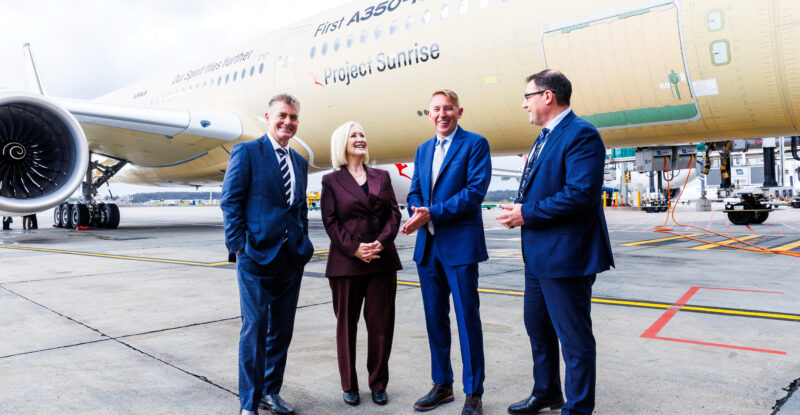 Executives are standing in front of a Qantas aircraft at Melbourne Airport.