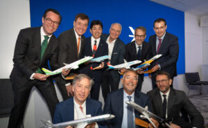Embraer announces commercial jet sales at the Farnborough International Airshow as various executives pose for a photo holding model aircraft.