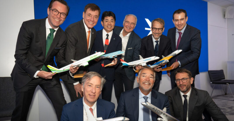 Embraer announces commercial jet sales at the Farnborough International Airshow as various executives pose for a photo holding model aircraft.