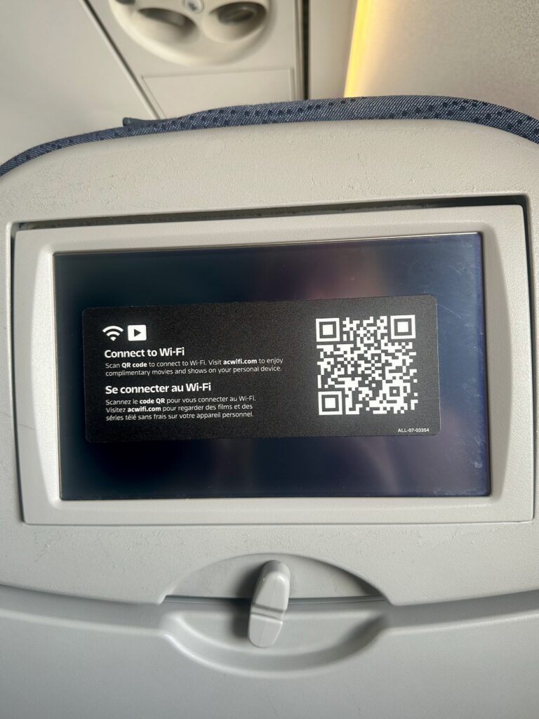 Black seatback screen with a 'connect to Wi-Fi' QR code sticker on it.