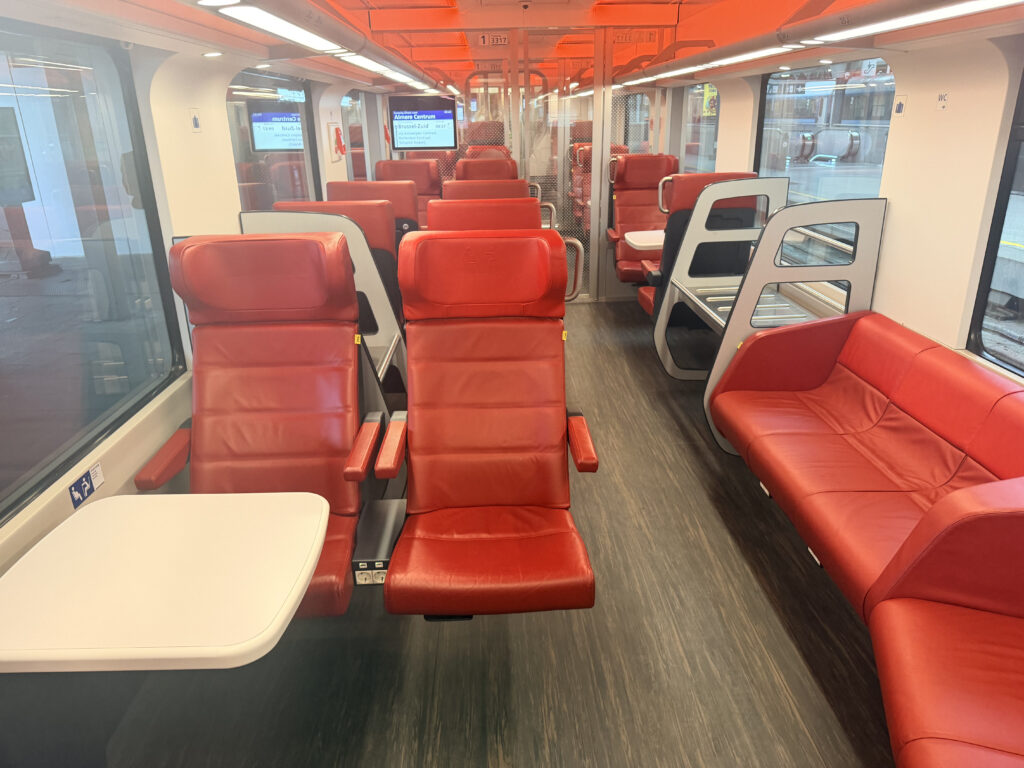 Red benches sit to one side of the rail car and seats of two sit on the other side with a table.