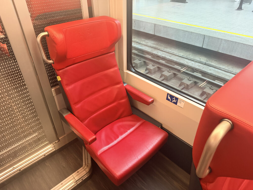 A decent sized red seat is sitting solo next to a large window.