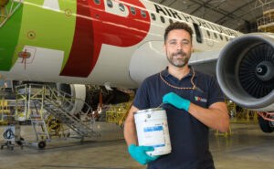 A man is holding up a container of AkzoNobel Aerospace Coatings’ Aerobase UPD formulation in front of a TAP aircraft.