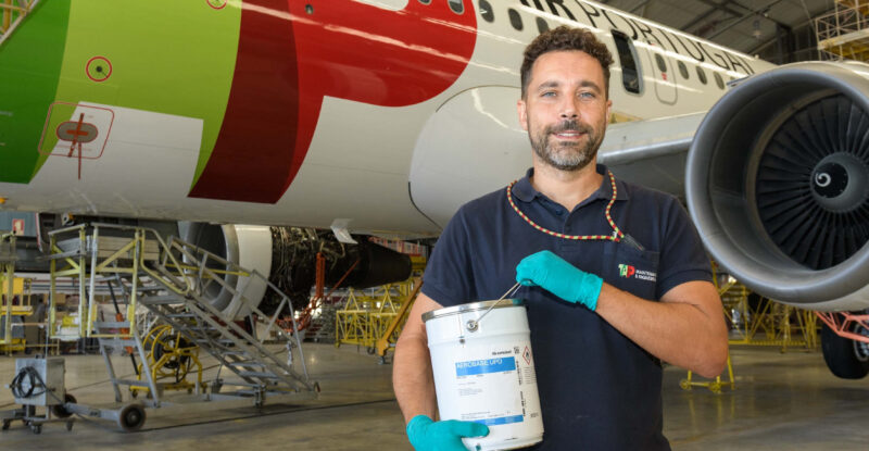 A man is holding up a container of AkzoNobel Aerospace Coatings’ Aerobase UPD formulation in front of a TAP aircraft.
