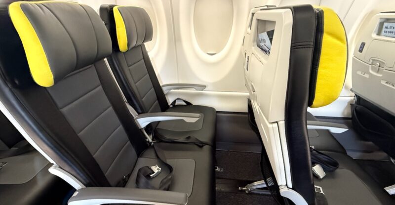 Seat duo on left side of A220. Seat are grey with yellow trim on the headrests.