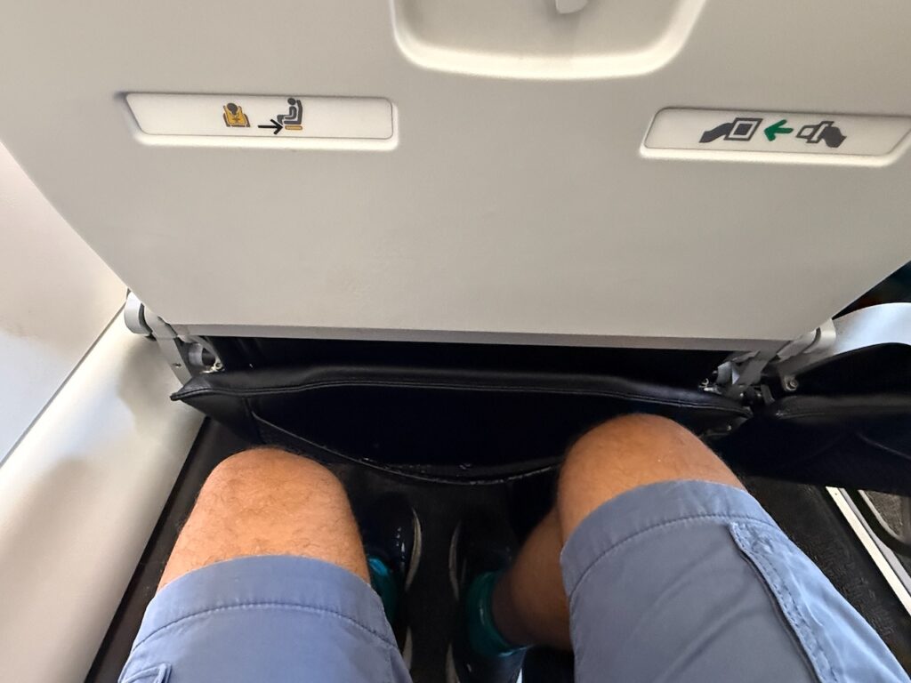 A man's knees are seen a decent distance from the seat in front of him.