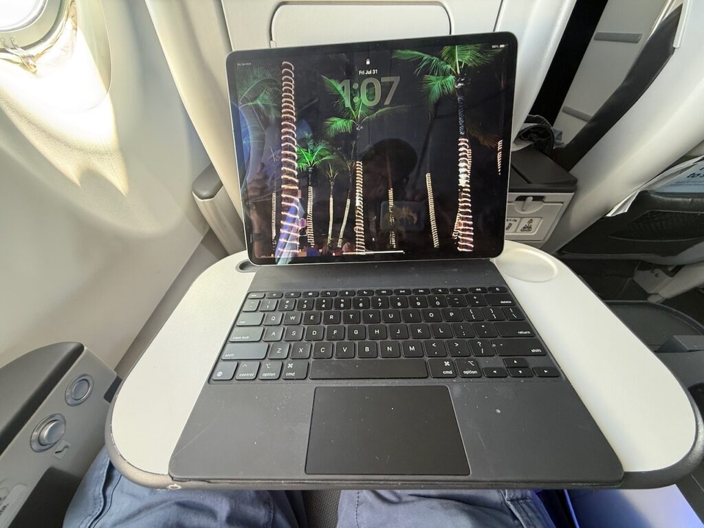 An iPad and keyboard sits on the aircraft tray table.
