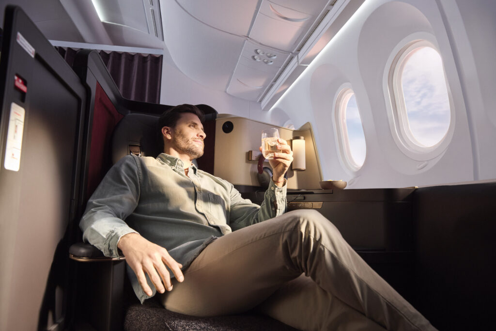 A male passenger, in an INSIGNIA window seat, enjoys a glass of wine, while looking out of the cabin window on the Avianca 787