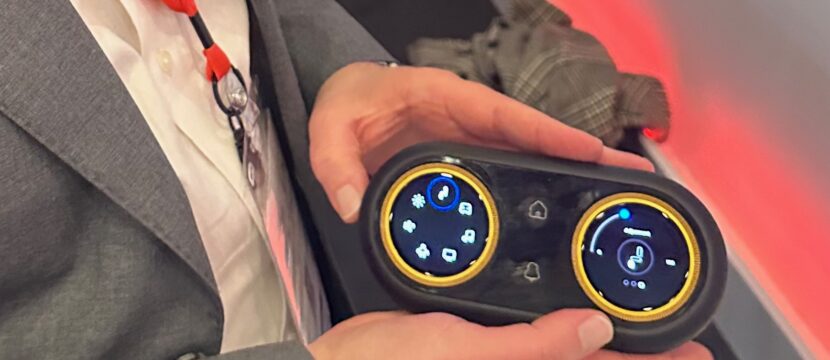 RAVE Aerospace's Ben Asmar holds up the new IFE and seat controller concept, which offers more accessible jog wheels as opposed to a touchscreen