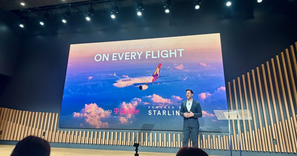 Edge speaks on stage whilst a giant screen advertises Starlink on every flight
