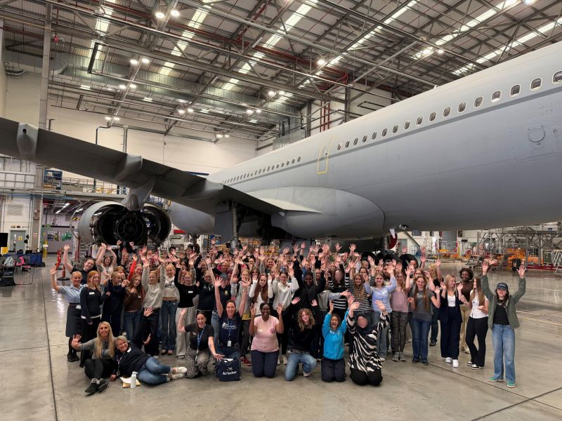 The attendees of the Girls in Aviation day pose for a photo with an aircraft in a hanger.