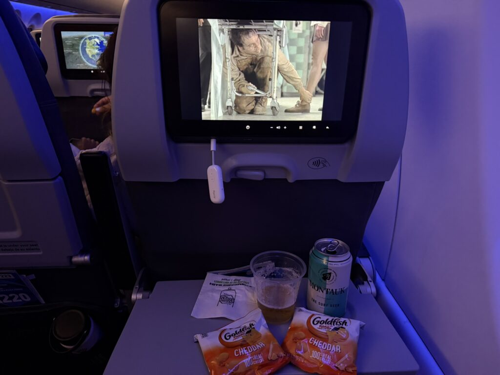 Beer and snacks on the tray table, while a move plays on the seatback screen