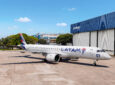 LATAM E195-E2 outside a hangar at the Embraer factory. The aircraft features a slimline antenna atop its fuselage to support inflight connectivity.
