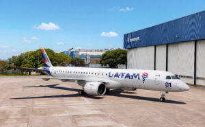 LATAM E195-E2 outside a hangar at the Embraer factory. The aircraft features a slimline antenna atop its fuselage to support inflight connectivity.