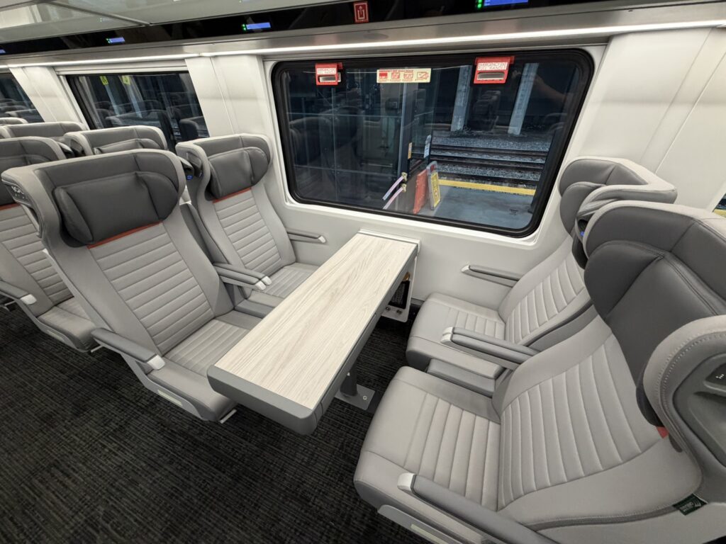 A quad of Coach Class seats sit empty on the Airo trainset. A table is between them with two seats on either side