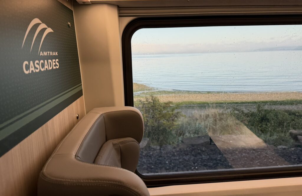 The words Amtrak Cascades on a green divider, right behind the large privacy wings of a seat on the Airo trainset
